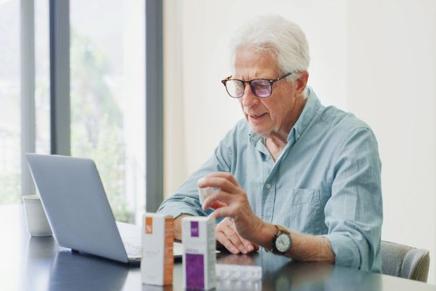 An elderly man ordering medications on his laptop