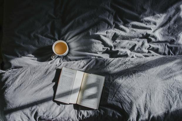 a book and cup of coffee on a gray bedspread