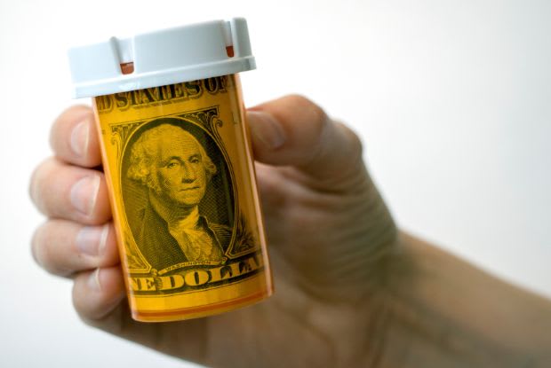 A hand holding a prescription bottle with a dollar bill inside
