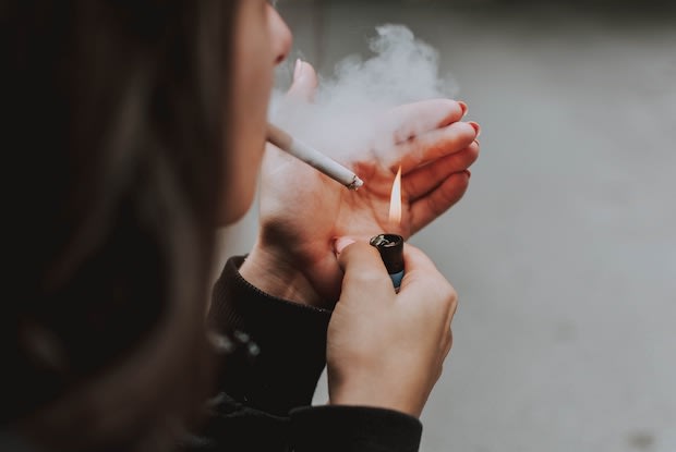 Person holding hand up while lighting cigarette with lighter