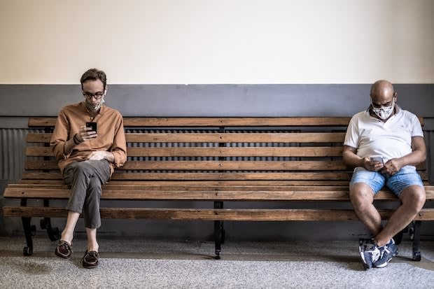 two people sitting on a bench, looking at their phones