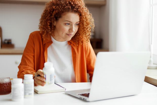 A woman looking at her laptop and holding medication