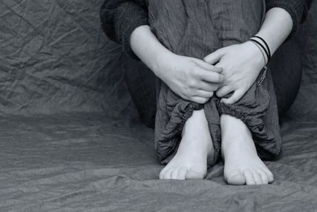 A black and white image of someone sitting on the floor holding their legs