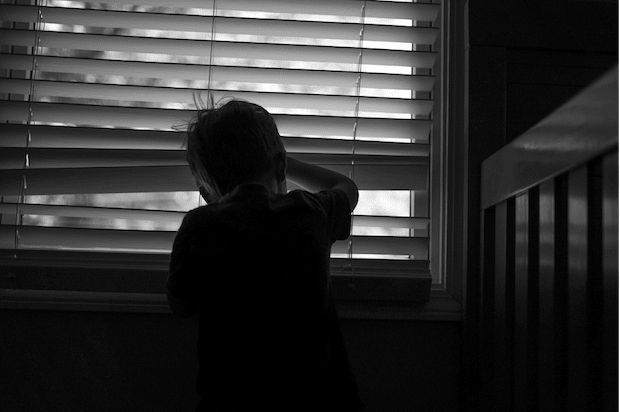 a child peeking out a window through the blinds