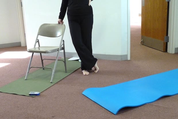 Barefoot person wearing all black leaning on chair placed on top of yoga mat