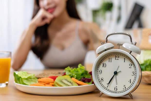 an alarm clock placed in front of a plate of food with a person in the background
