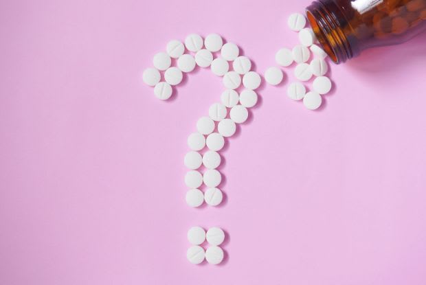 A question mark made up of white tablets on top of a pink background