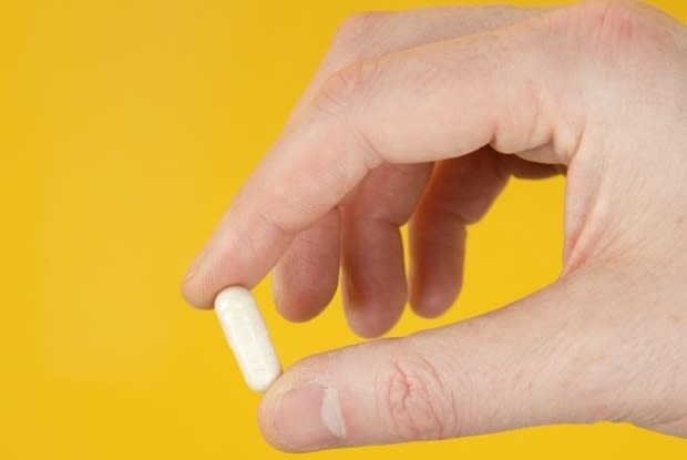 a hand holding a white pill on a yellow background