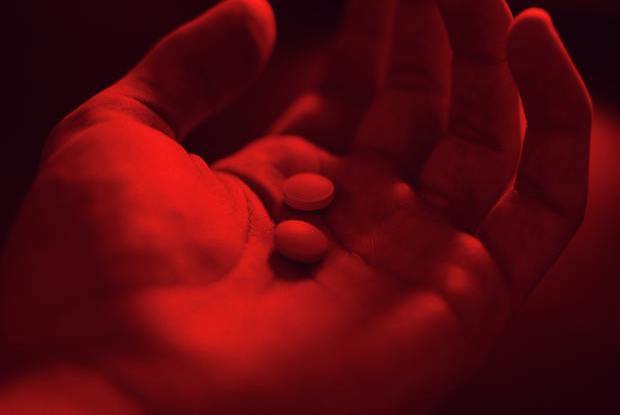 a hand bathed in red light with two pills in the palm