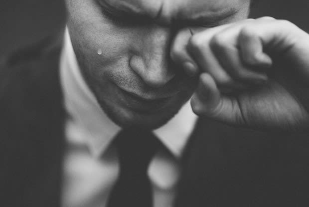 Grayscale image of man in suit wiping tears from eye