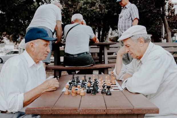 two older men playing chess against each other at a park