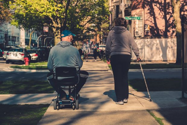 a man in a wheelchair and a woman walking with a cane