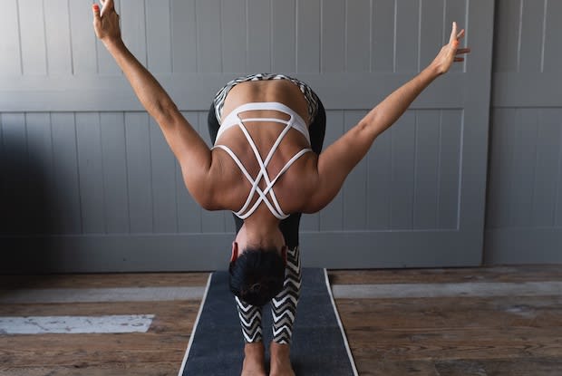 Woman on yoga mat in a forward fold with arms up