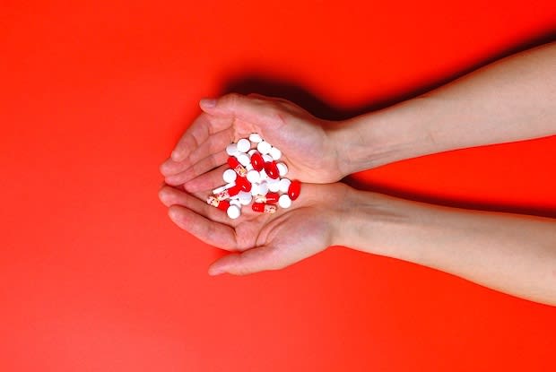 hands holding variety of pills with orange background