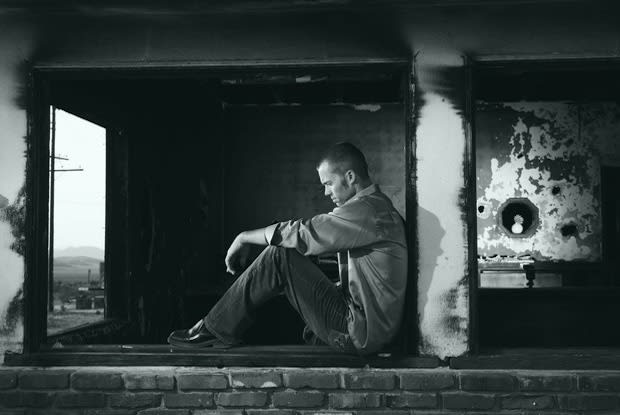 Black and white photo of a man sitting on a wall looking downwards