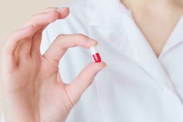 A hand holding up a white and red medication pill