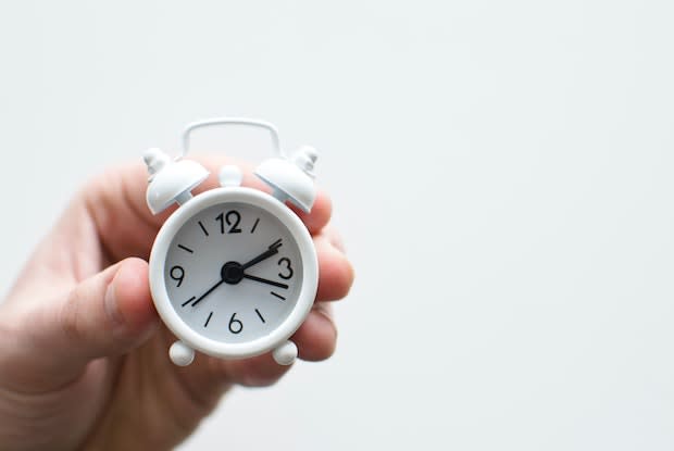 a hand holding an analog alarm clock