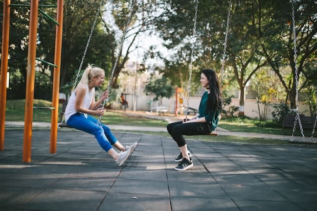 two girls talking to each other while sitting on swings