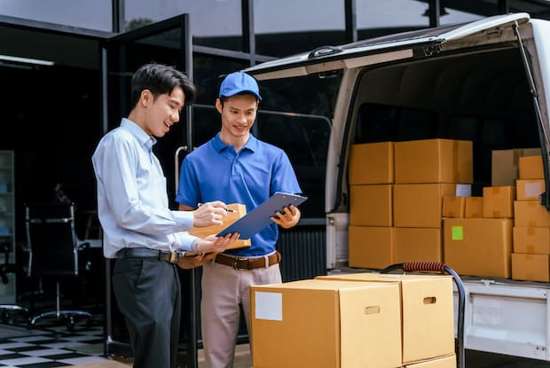 a delivery driver speaking to another person with many cardboard packing boxes in the shot