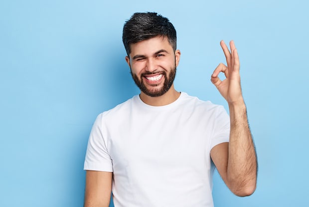 a smiling man holding up an “okay” sign. width=
