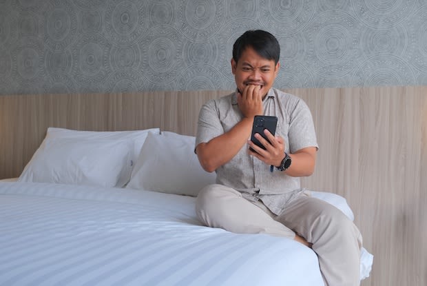 a man checking his phone while sitting on his bed