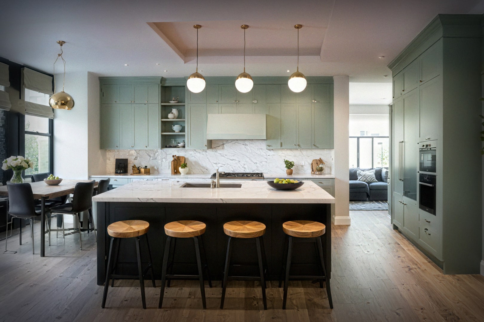 Open-concept kitchen featuring green cabinetry, marble counters, large island, and wooden bar stools