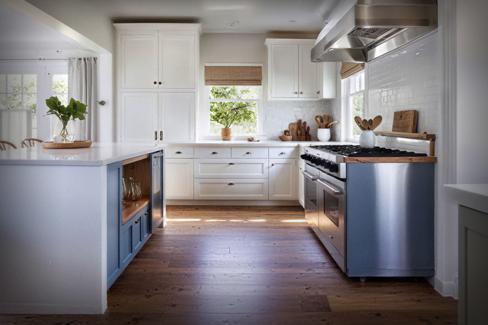 Bright white transitional kitchen with navy island, farmhouse sink, and natural wood flooring