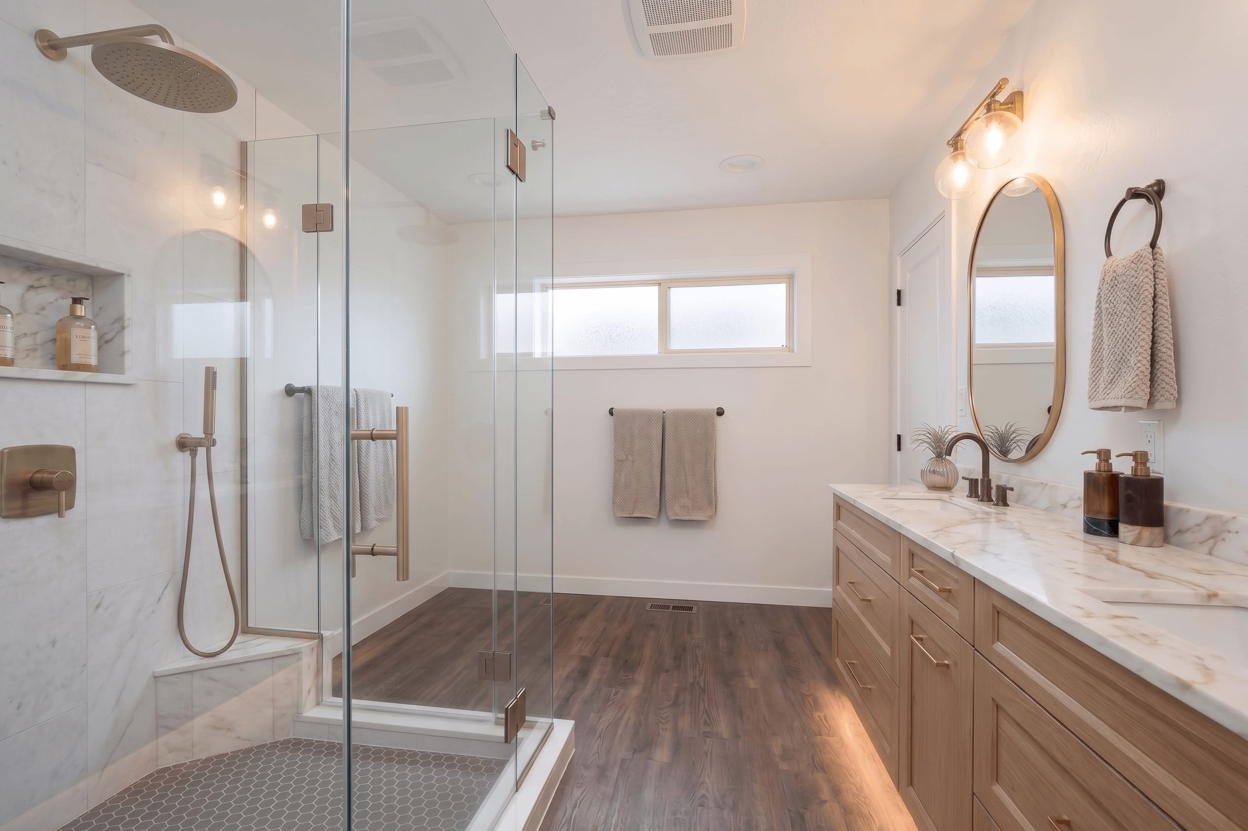 Warm Oak & Brass Spa Sanctuary — custom natural oak double vanity, under-cabinet LED lighting, Calacatta marble countertop, and gold oval mirrors in Washington DC bathroom remodel