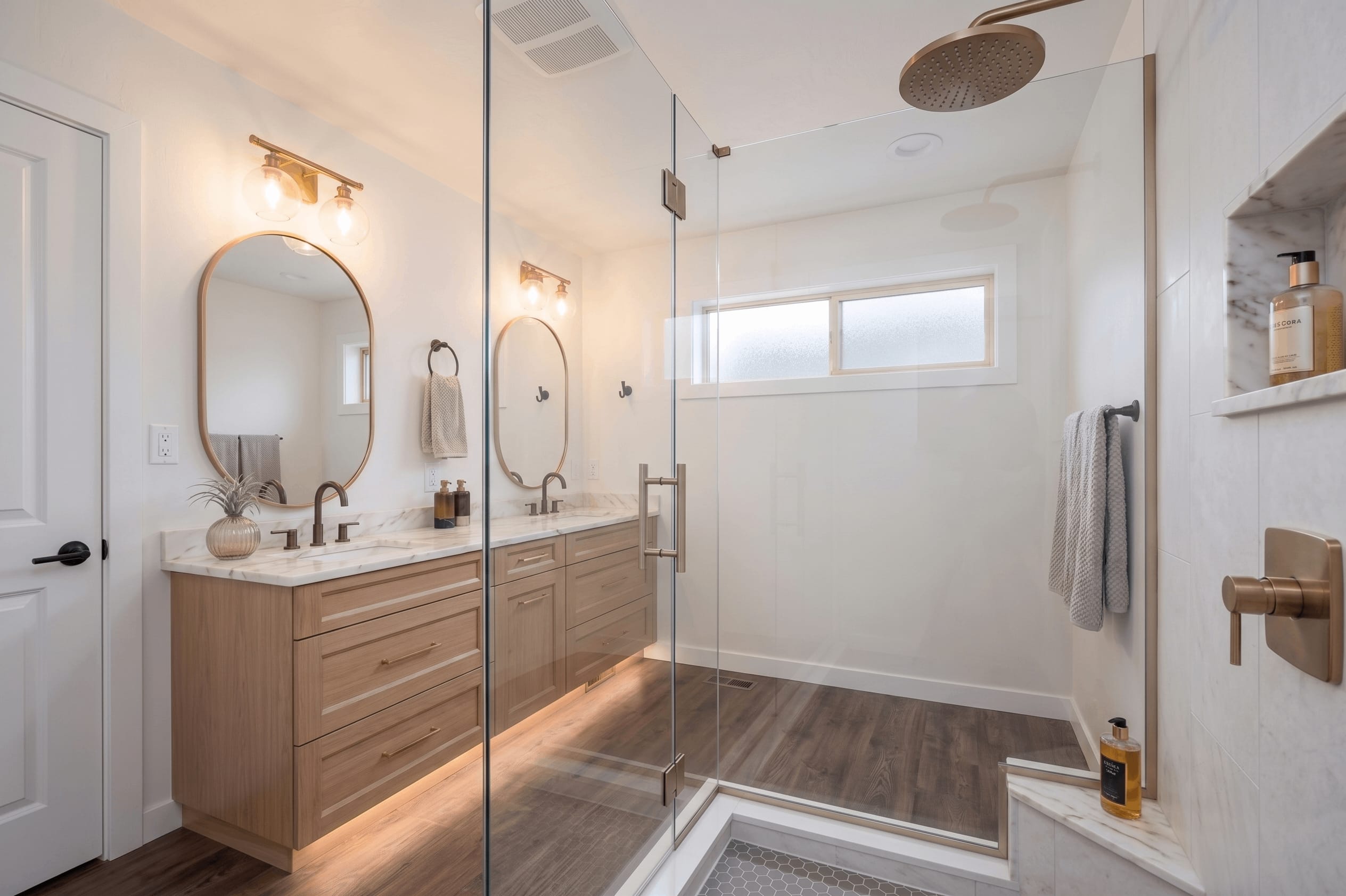 Warm Oak & Brass Spa Sanctuary — frameless glass walk-in shower with brushed brass rain showerhead, Calacatta niche, and dark hex tile floor pan in Washington DC