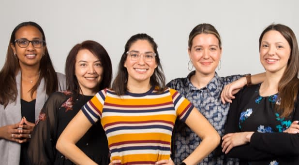 An african american woman, a latina woman and three white women stand smiling in powerful poses