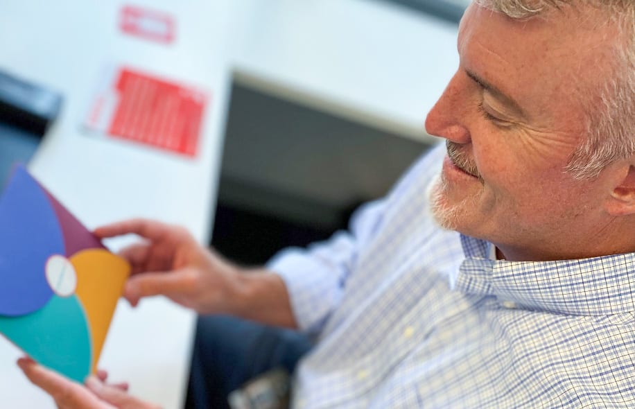 Smiling man with a grey goatee looking at a mulitcolored envelope