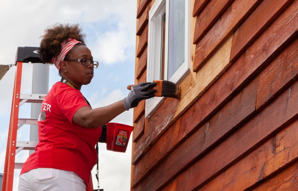 An african american woman in a red volunteer shirt paints a house they are building for veterans