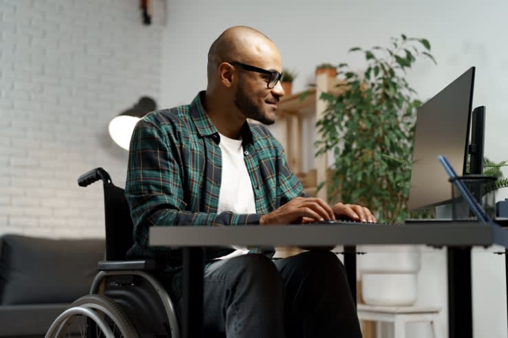 Disabled young african american man in wheelchair using computer while sitting at his working table