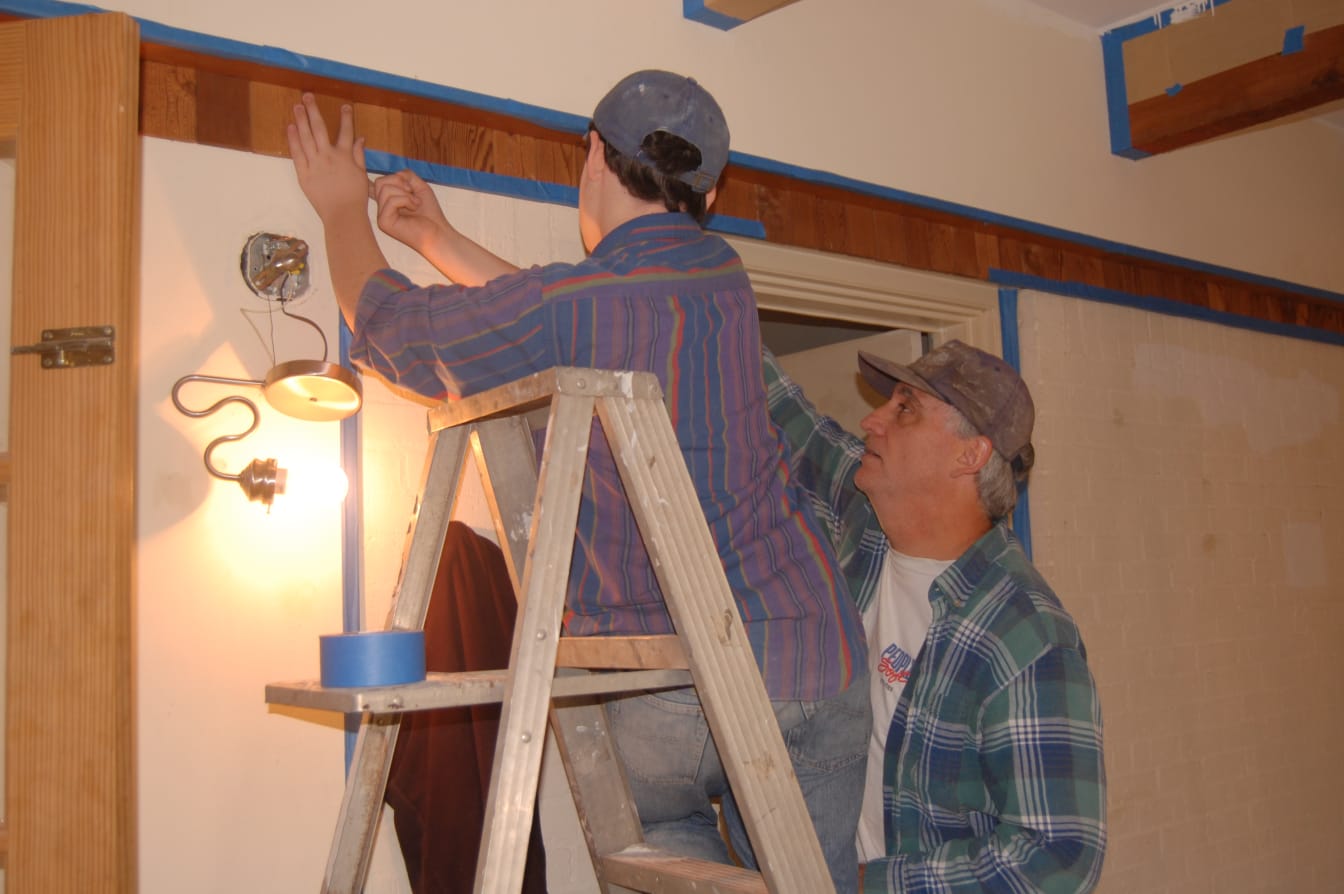 Rick Howard (right) and his son put up masking tape in preparation for painting the walls.