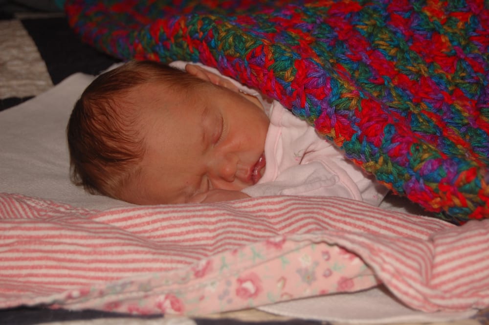 Newborn Hosanna sleeping, tucked under a brightly colored crocheted blanket