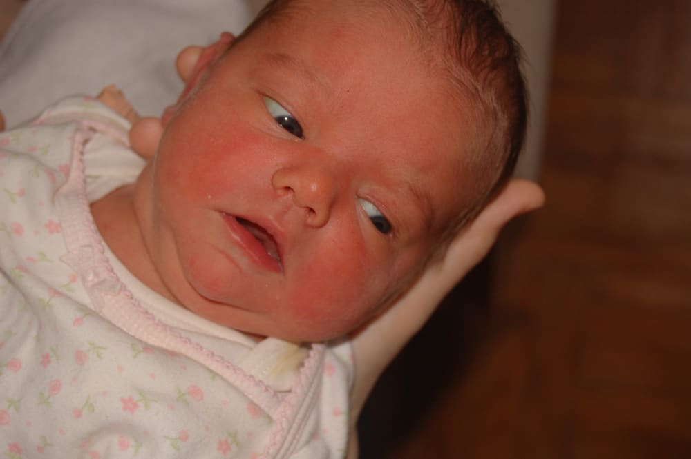 Close-up of newborn Hosanna's face, cradled in a hand and wearing a floral onesie