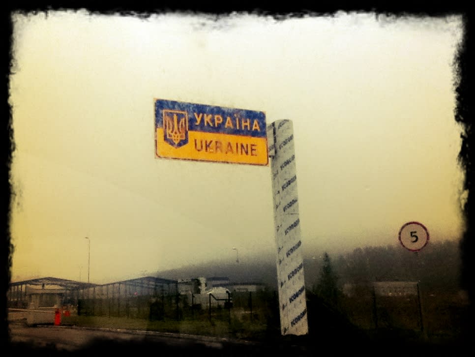 Roadside border sign reading Україна and Ukraine at a foggy frontier crossing