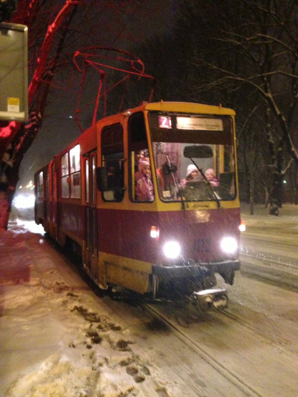 Children sitting in the cab of a red and cream Ukrainian tram on a snowy street at night