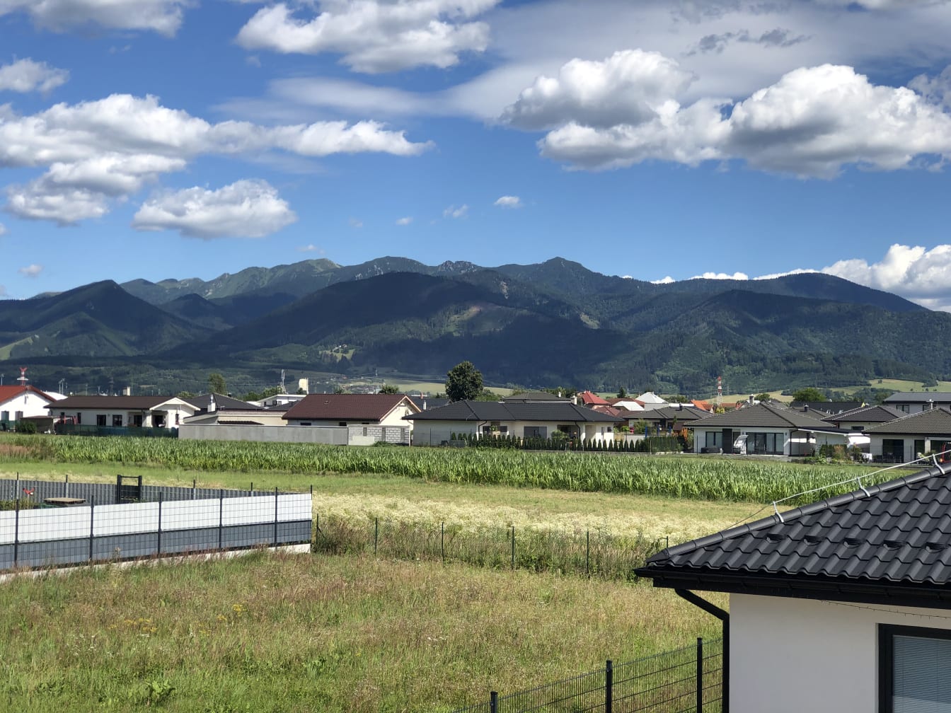 View from the terrace across green fields toward a mountain range under a blue sky, with village rooftops in between