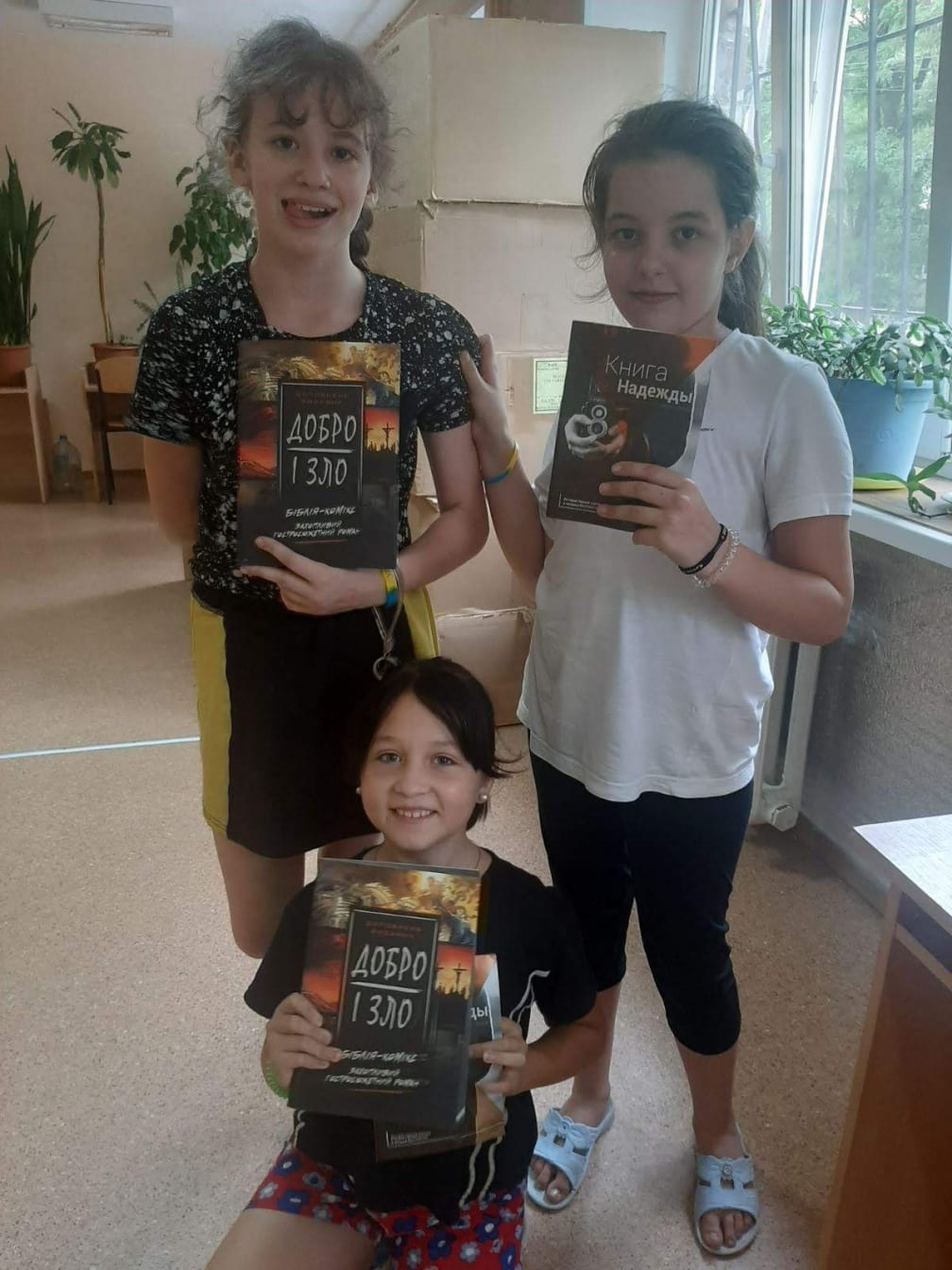 Three Ukrainian girls indoors holding up copies of the Good and Evil book (Добро і Зло)