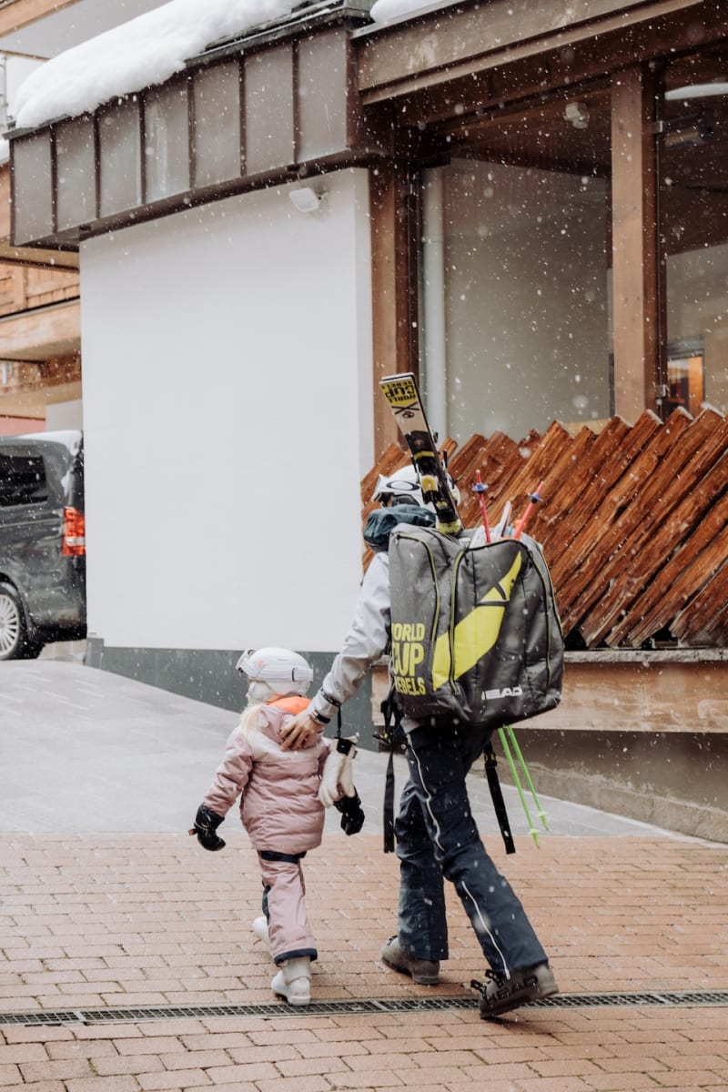 Ein Erwachsener und ein Kind gehen im Schnee zum Glemmtalerhof in Hinterglemm, um Ski zu fahren.