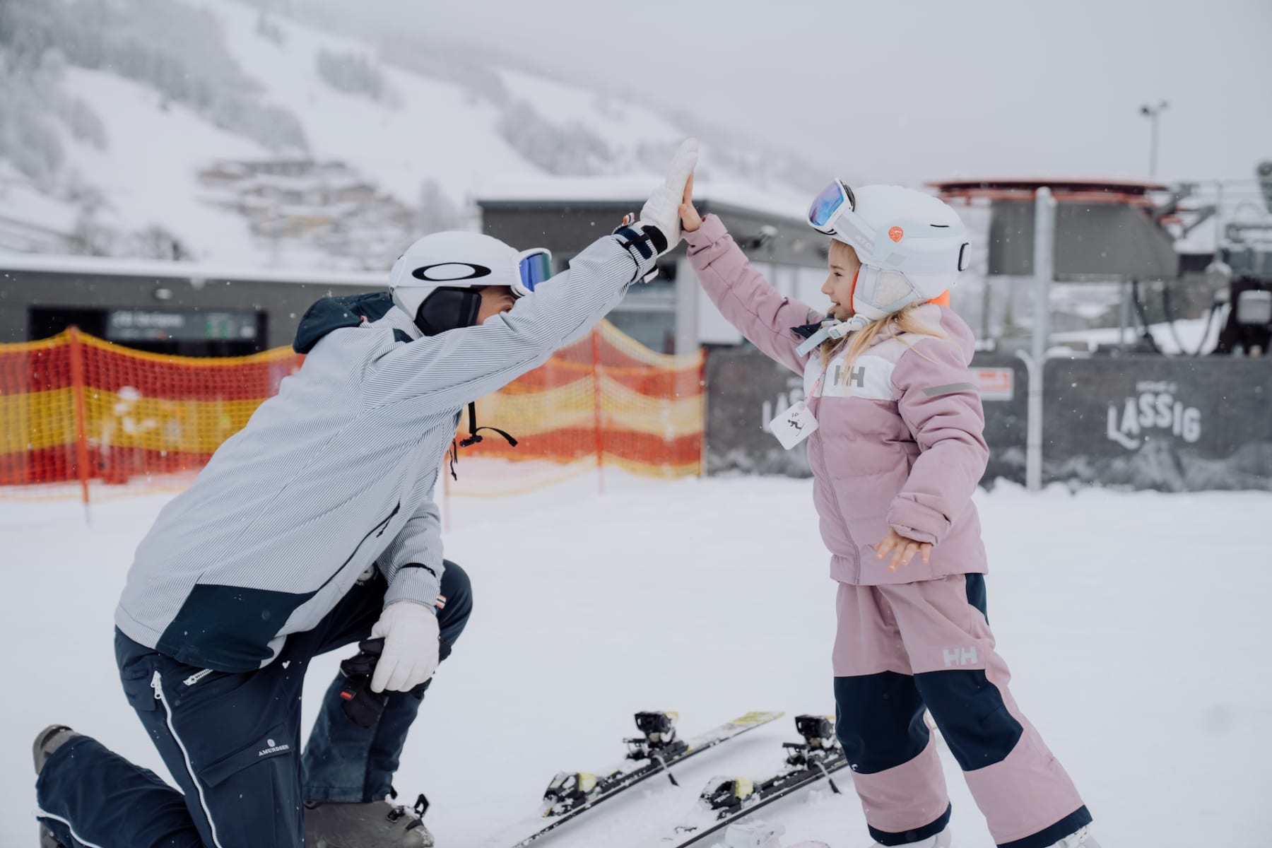 Ein Kind und ein Erwachsener feiern im Schnee vor dem Glemmtalerhof in Hinterglemm mit Skiausrüstung.