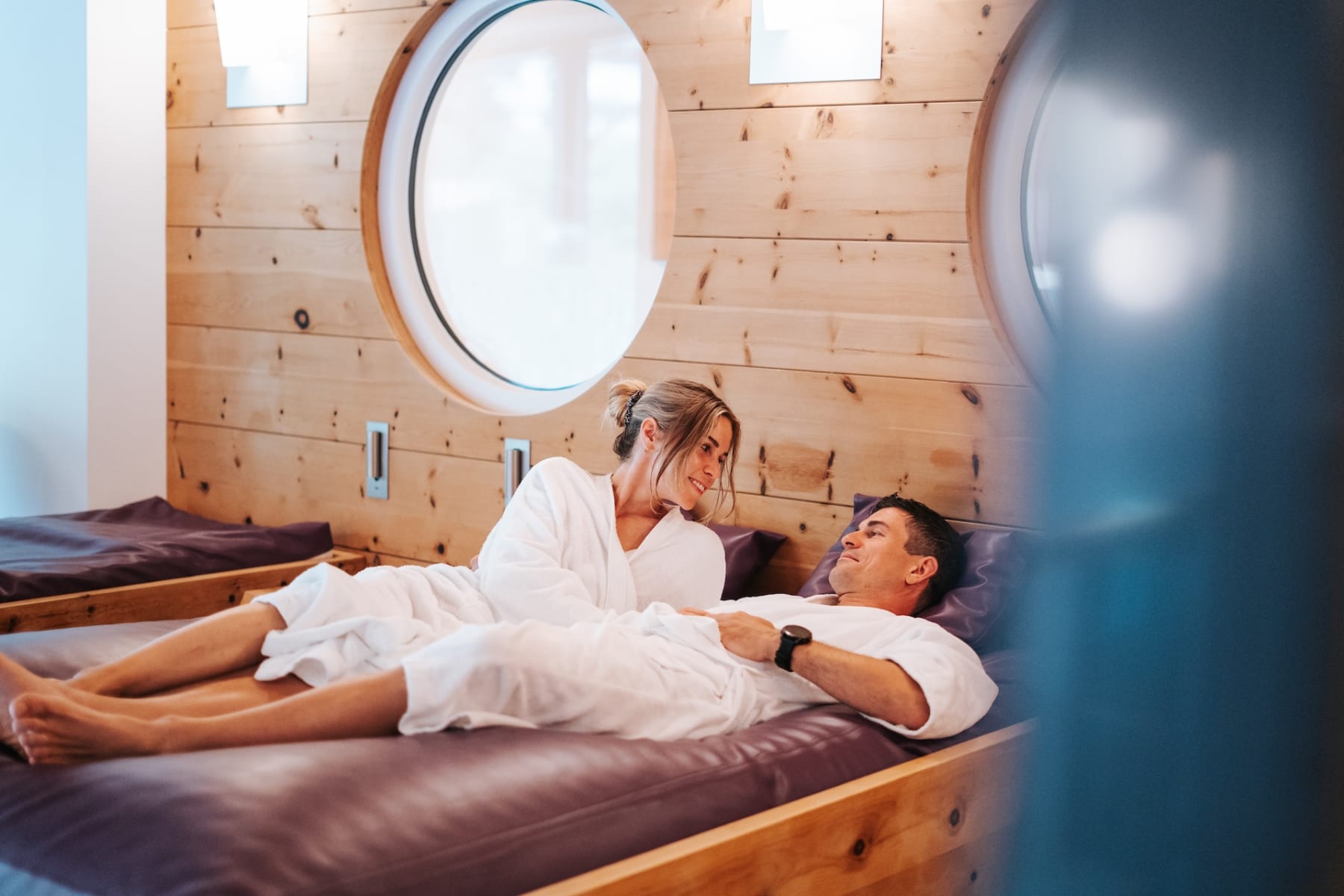 Ein Paar in Bademänteln entspannt im Glemmtalerhof in Hinterglemm. Gemütliche Atmosphäre mit Holzverkleidung.
