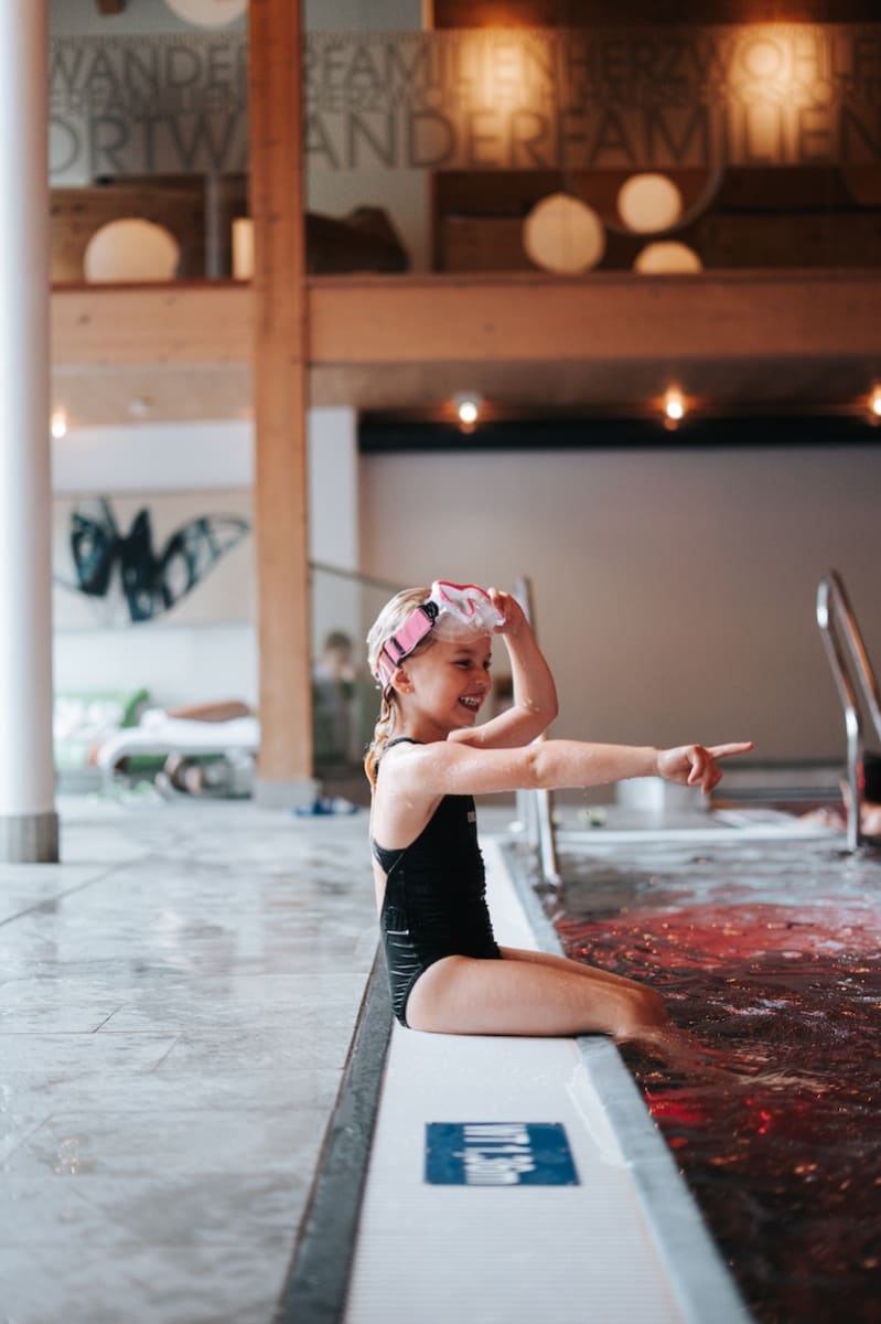 Ein Mädchen mit Schwimmbrille spielt am Rand des Beckens im Glemmtalerhof in Hinterglemm.