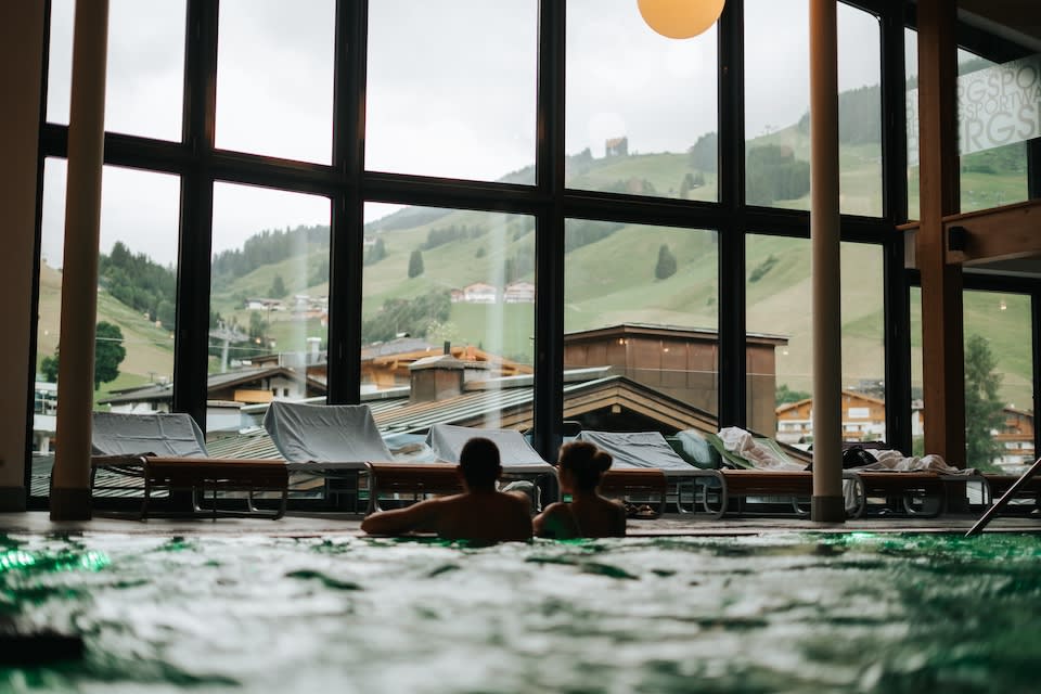 Ein Pool im Glemmtalerhof mit Blick auf die Berge und das Glemmtal, entspannte Atmosphäre mit Gästen im Wasser.