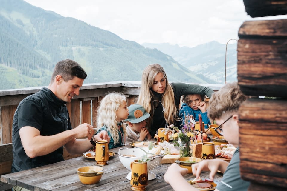 Eine Familie genießt eine Mahlzeit im Glemmtal mit Blick auf die umliegenden Berge. Gemütliche Atmosphäre.