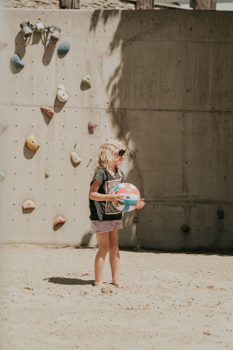 Ein Mädchen im Sand mit einem Ball, hinter ihr eine Kletterwand. Glemmtal Abenteuer.