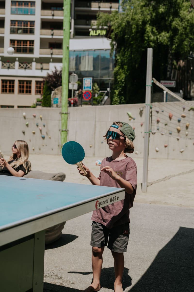 Ein Junge spielt Tischtennis im Glemmtal, während im Hintergrund das Gebäude Glemmtalerhof sichtbar ist.