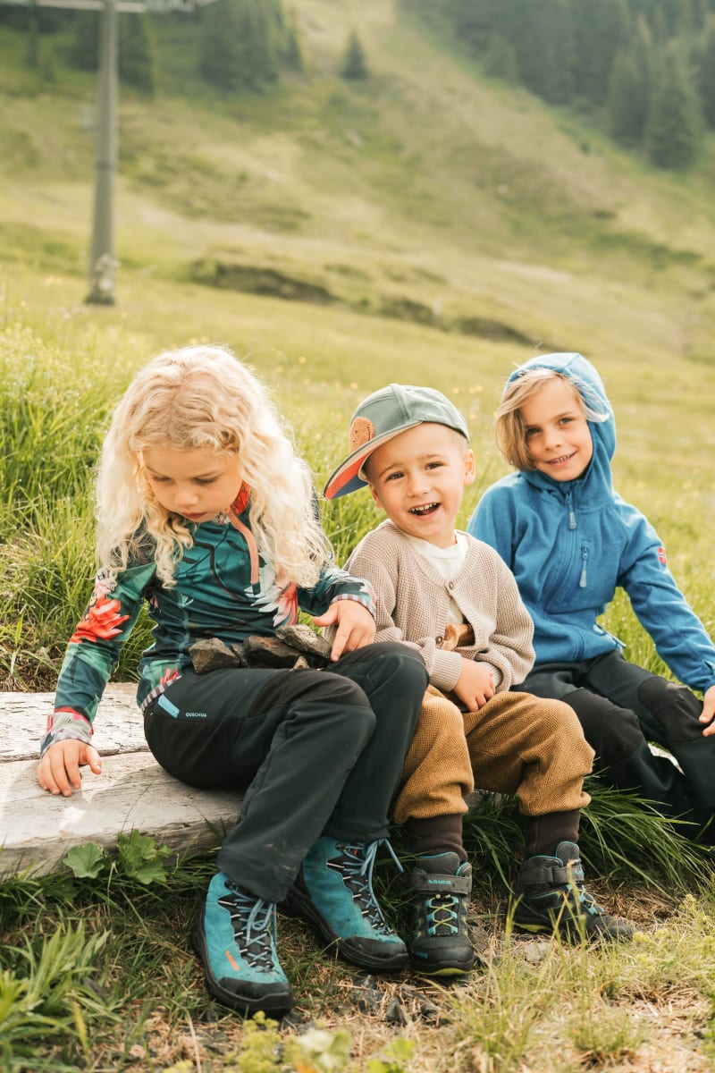 Drei Kinder im Glemmtal sitzen auf einem Baumstamm und genießen die Natur.