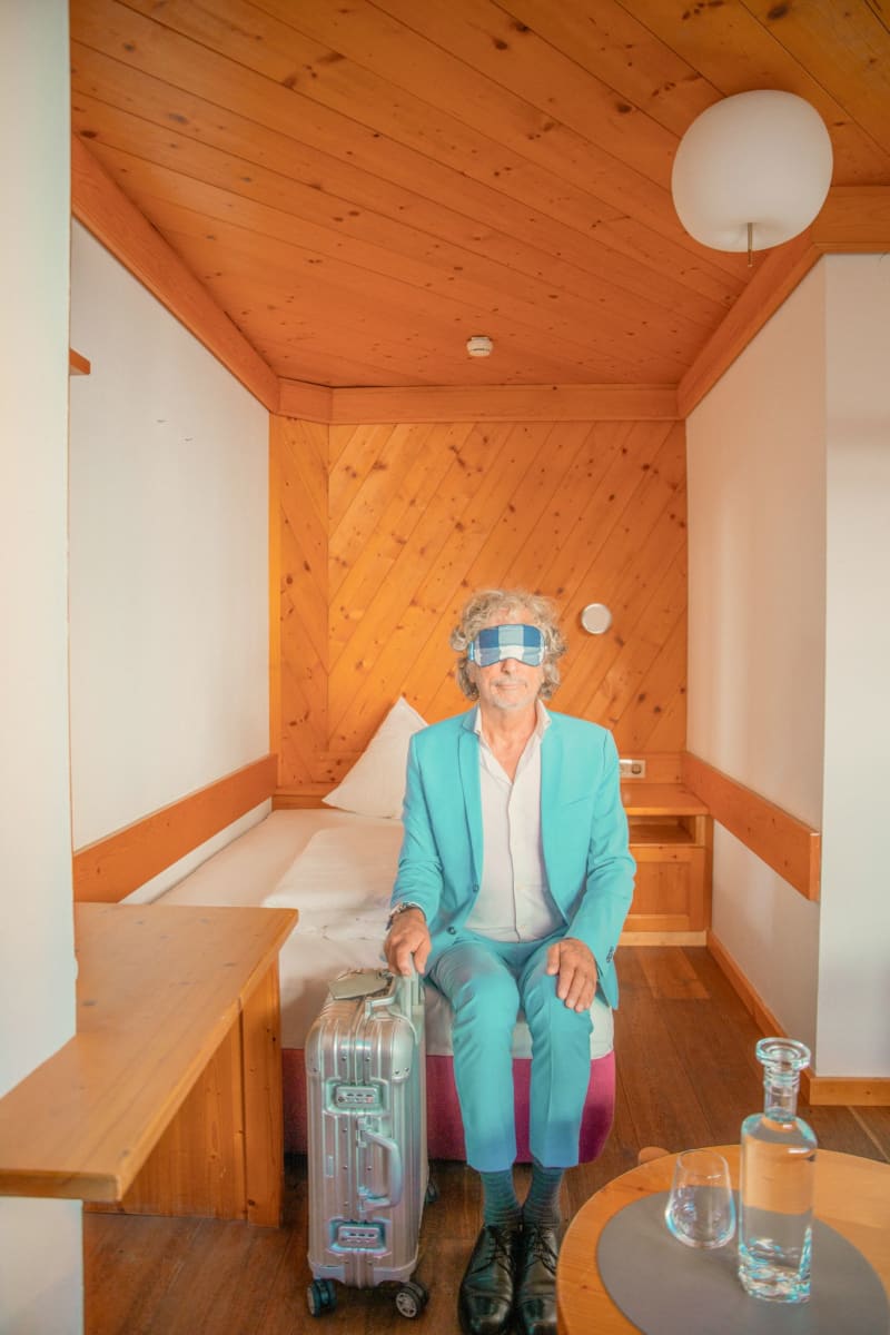 A man in a blue suit sits in Glemmtalerhof with a suitcase, ready for adventure.